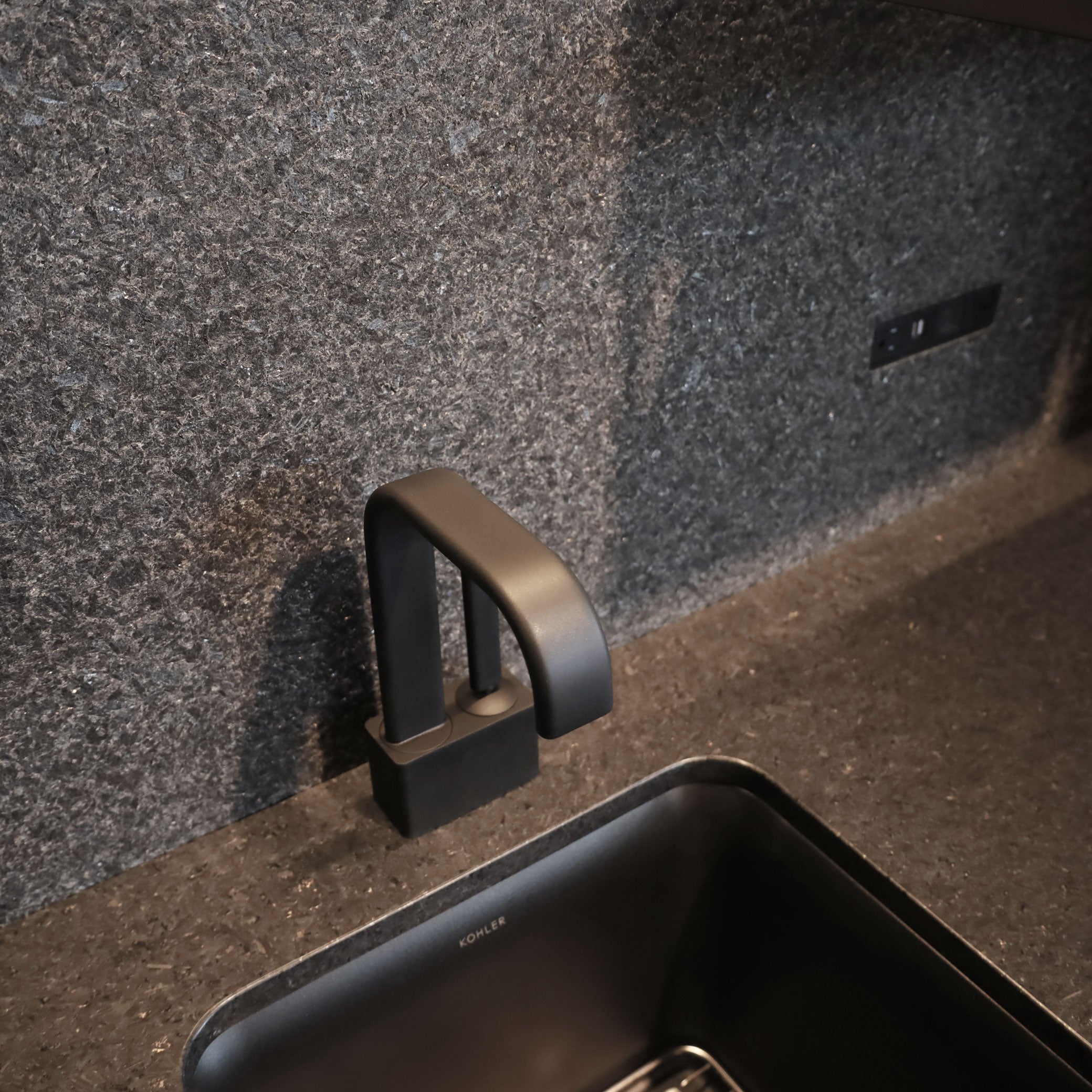 Une cuisine de luxe minimaliste comprend le BAR CABINET Humble Nature, un robinet noir mat sur pierre texturée foncée, un évier rectangulaire noir élégant et un réfrigérateur intégré pour un look moderne et homogène.