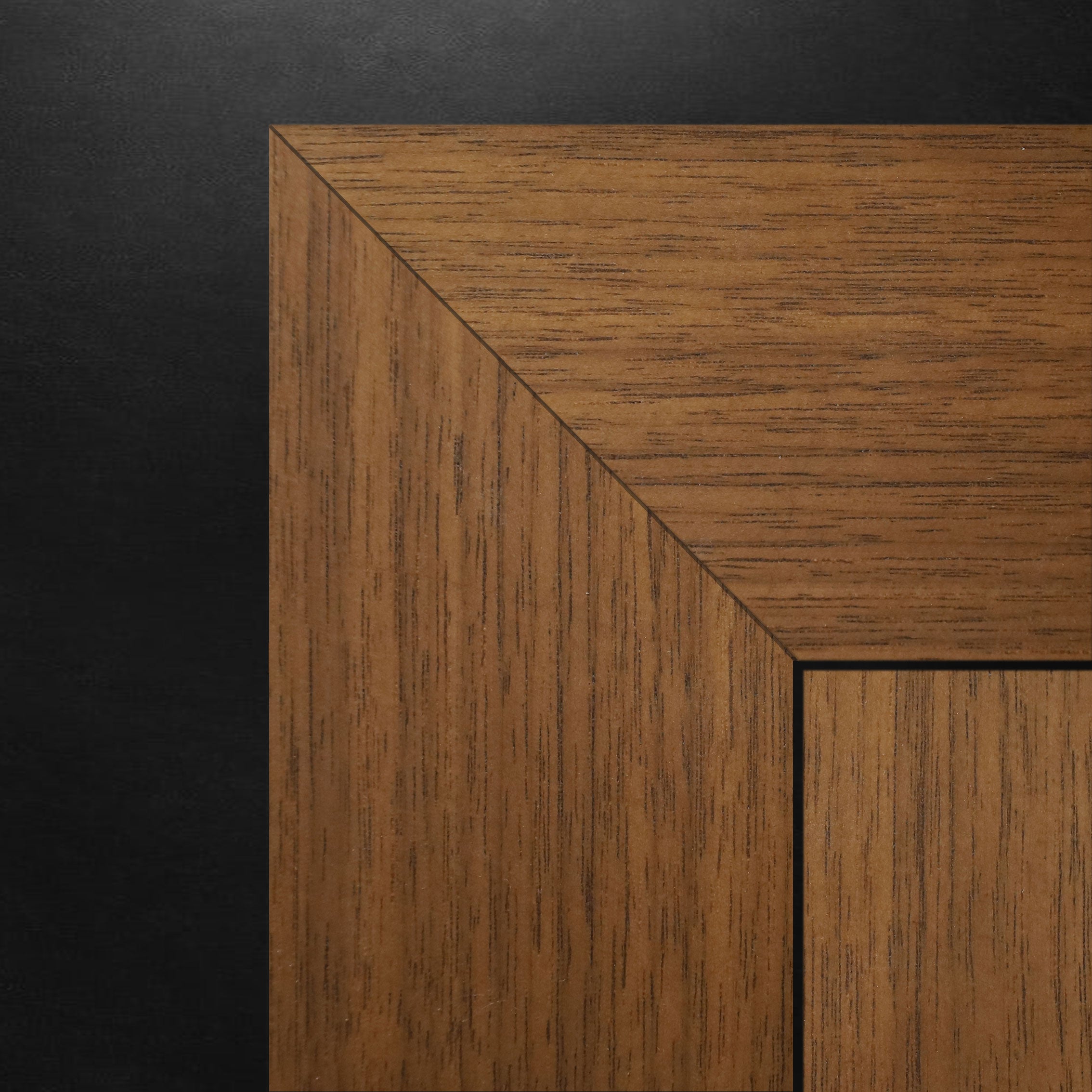 Gros plan dun coin de cadre photo en bois avec un grain de bois foncé sur fond noir. Son angle précis et son savoir-faire reflètent lélégance de la collection See & Pure - Ensemble de moulures Passage fini noyer de Humble Nature.