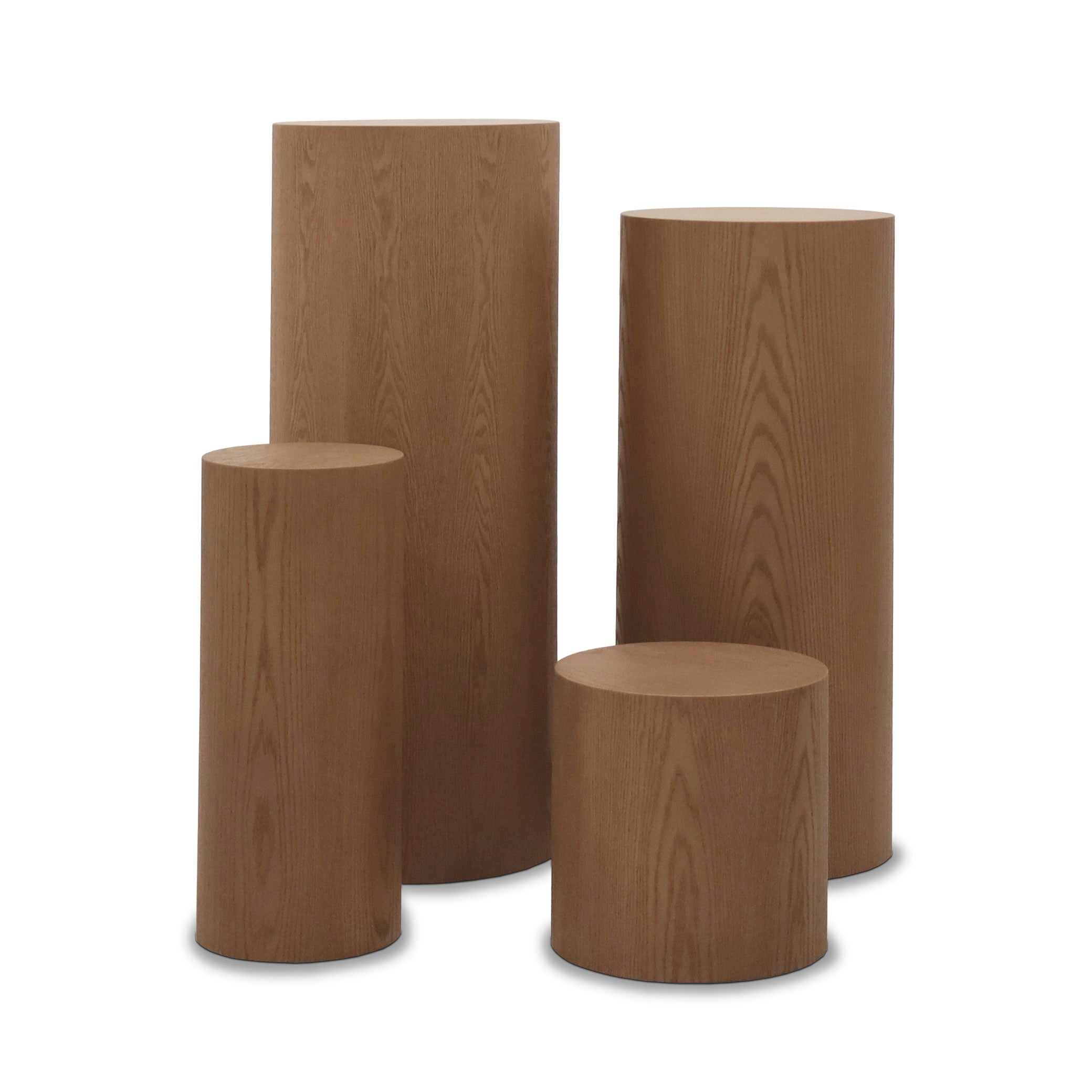 Quatre tables piédestal ronde en bois de différentes hauteurs de la collection « Table piédestal ronde 41 Essence | Saddle » de Humble Nature sont regroupés. Fabriqués avec un savoir-faire inégalé, leur teinte marron clair et leur motif de veinage de bois visible mettent en valeur l&