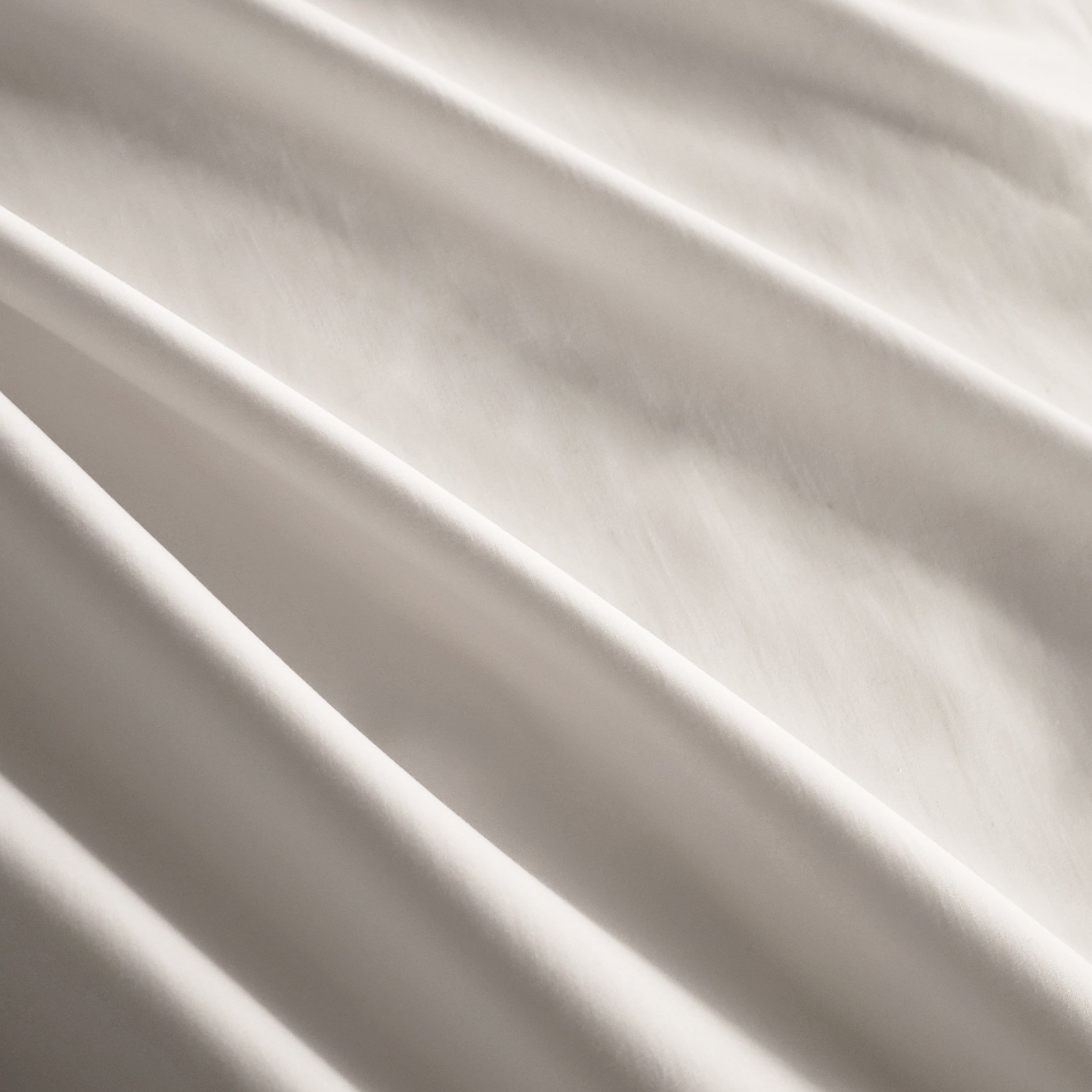 Gros plan sur un tissu en percale blanche à 400 fils, illustrant sa texture lisse et luxueuse. Conçu pour un confort exceptionnel et une élégance intemporelle, évoquant la qualité hôtelière raffinée de Humble Nature.
