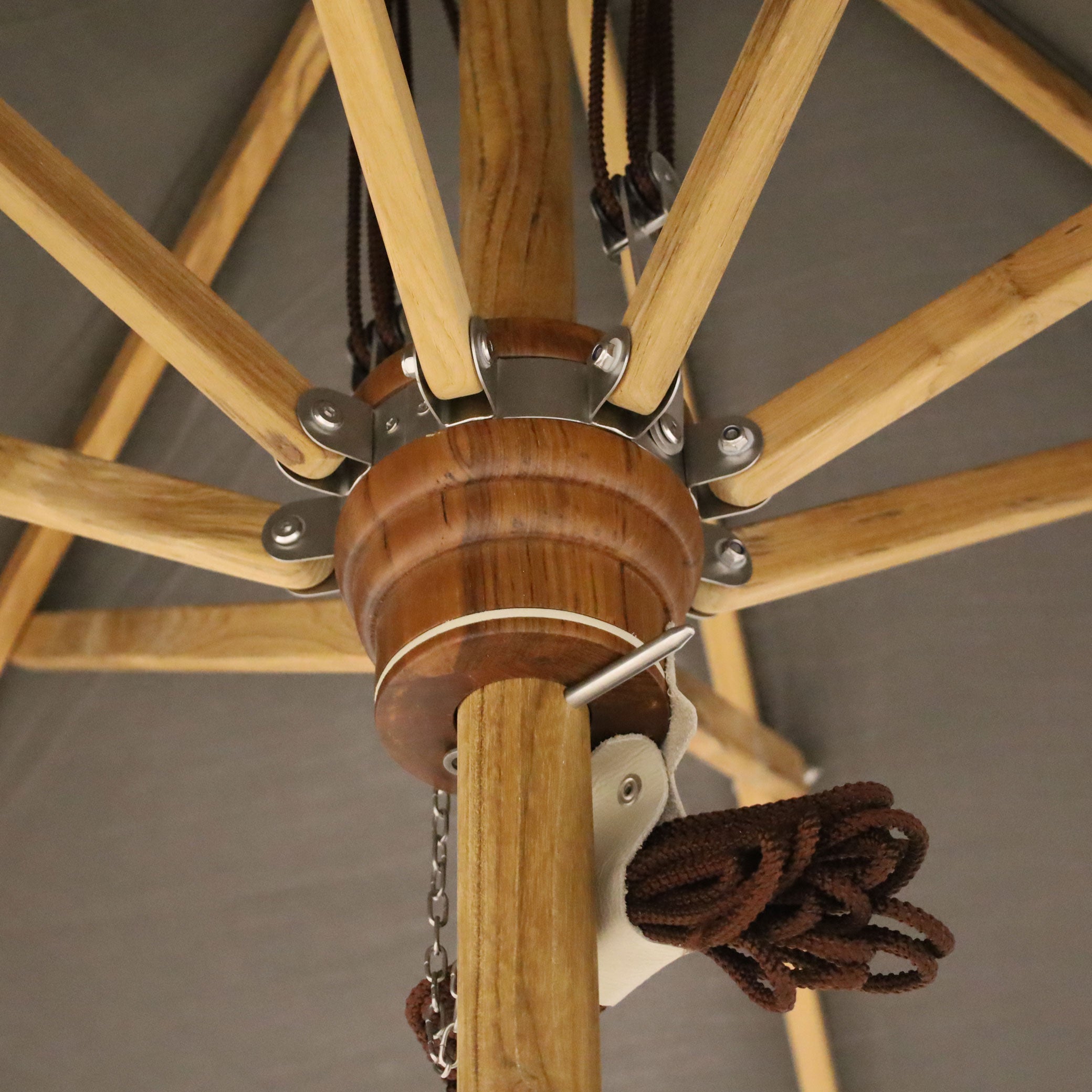Une vue rapprochée du parasol rectangulaire en bois de teck | Slate de Humble Nature révèle le moyeu central, les rayons et le système de poulie avec corde marron. Le bois de teck contraste magnifiquement avec la toile en tissu foncé de ce design contemporain.