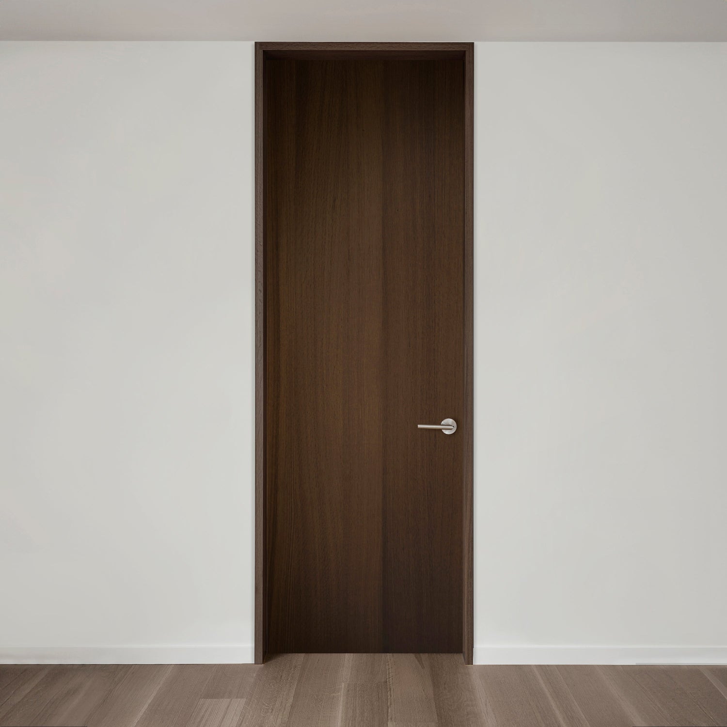 Une porte en bois haute et fermée avec une poignée argentée moderne placée dans un mur blanc uni et un parquet en bois clair.