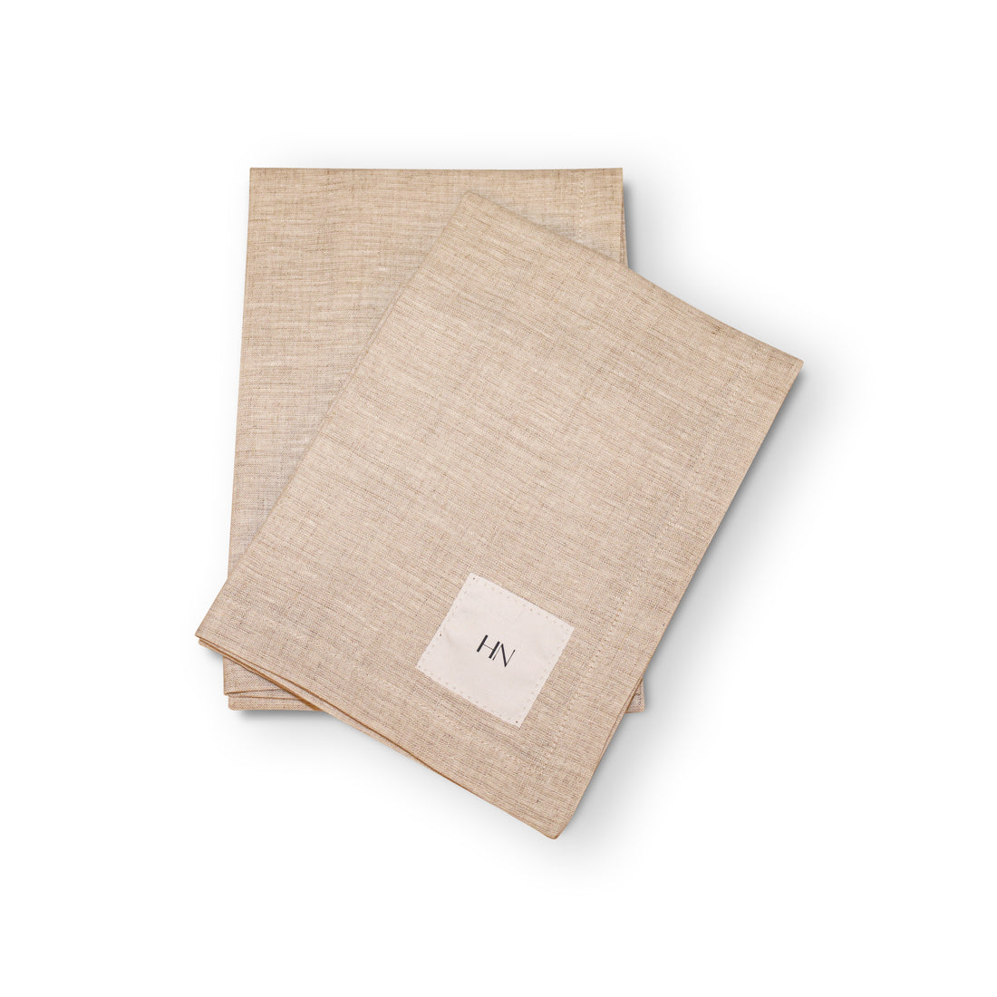 Deux serviettes en lin beige de la collection « Linge de table en lin | Ensemble de 2 | CLAY » de Humble Nature reposent soigneusement sur une surface blanche. Lune delles est ornée dun petit carré blanc avec le mot « HN » brodé dessus, dégageant une élégance intemporelle pour un look naturel et sophistiqué.