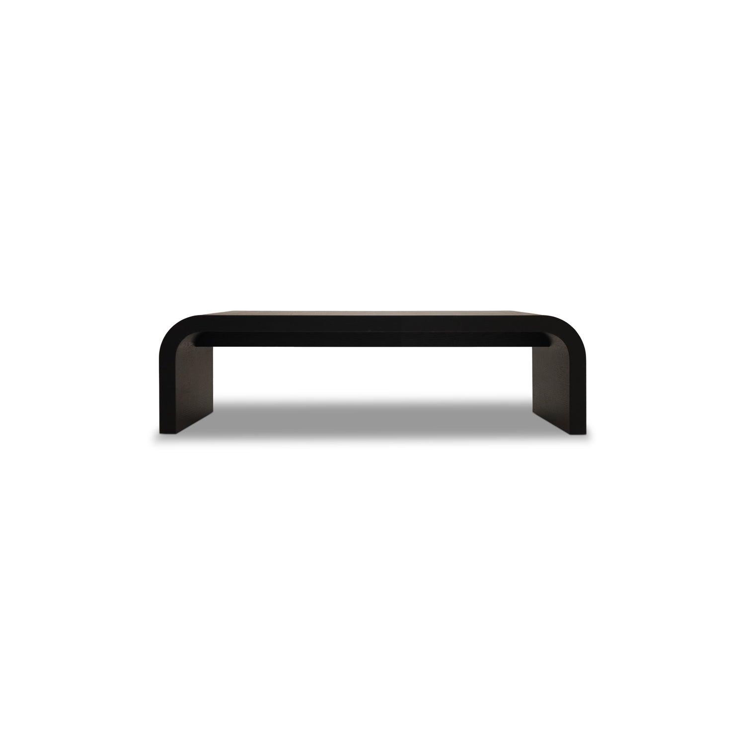 Le Banc 64 en bois Essence │ ONYX de Humble Nature est une banc noir minimaliste avec une surface rectangulaire lisse et des bords élégamment incurvés, reflétant la sophistication alors quelle se dresse gracieusement sur un fond gris clair.