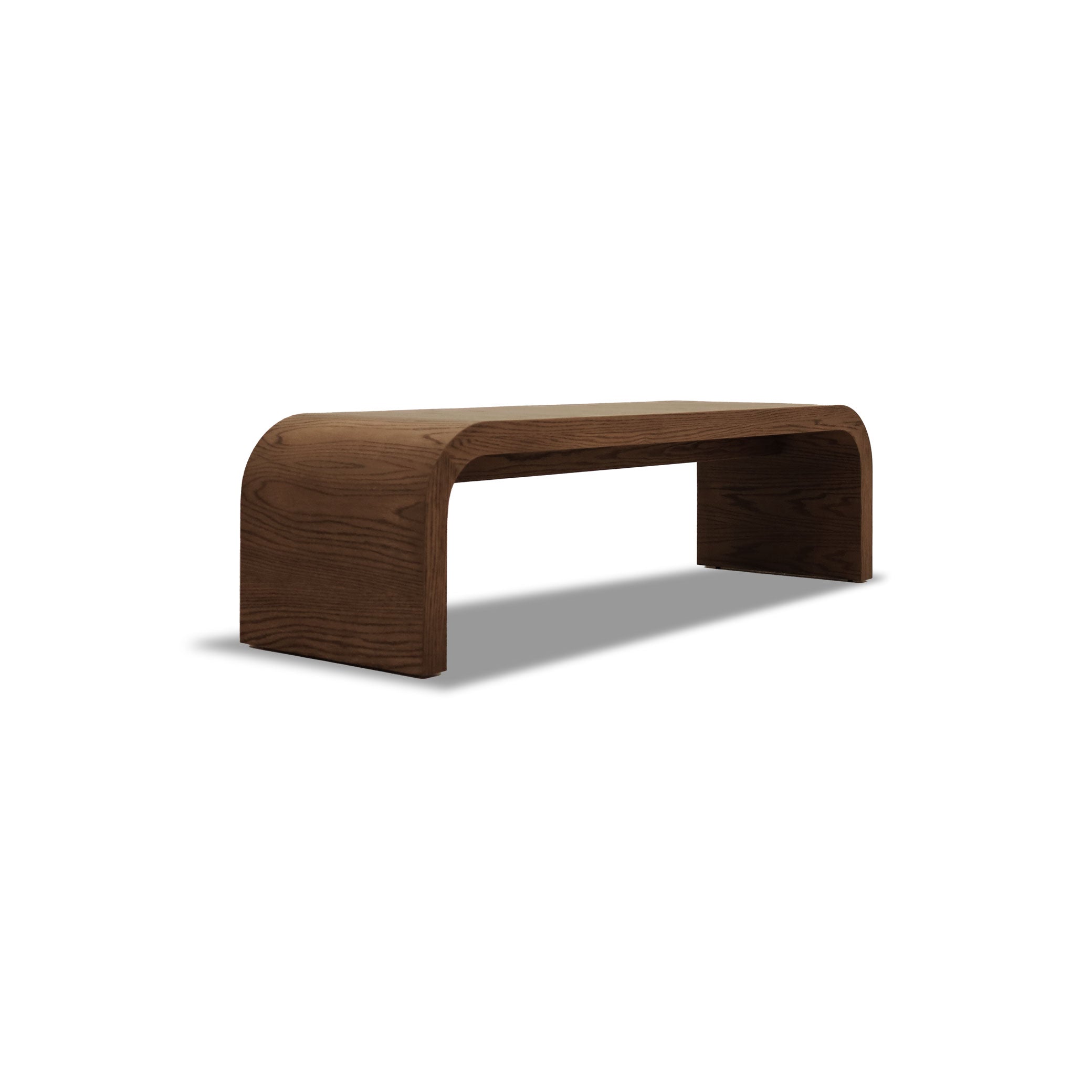 Le Banc 64 en bois Essence │ PECAN de Humble Nature est un banc en bois courbé au design minimaliste et à la surface lisse en chêne rouge riche, fabriqué à partir de bois massif durable. Sa structure élégante se détache sur le fond blanc.