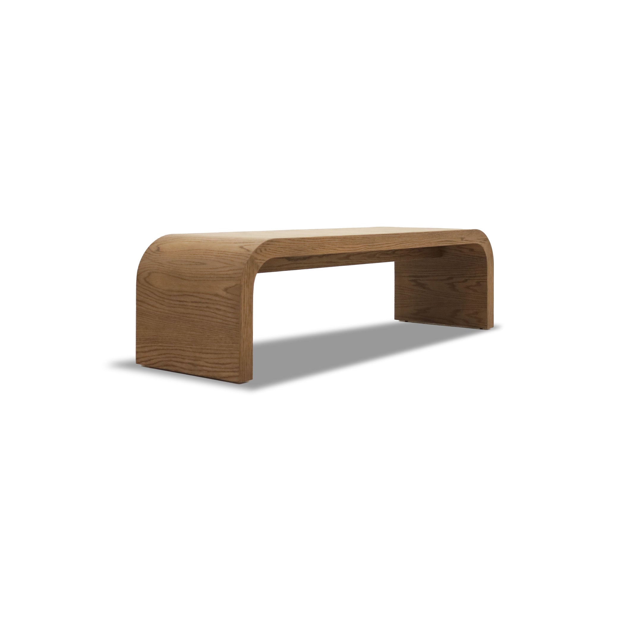 Le Banc 64 en bois Essence de Humble Nature, bas et minimaliste, aux bords lisses et incurvés et à la finition grain de bois naturel, se dresse sur un fond blanc.