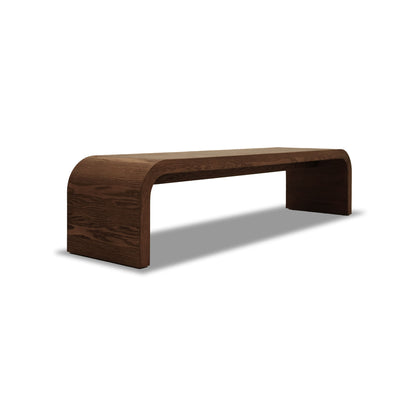 Le Banc 80 en bois Essence │ PECAN de Humble Nature est un banc en bois élégant et moderne fabriqué en chêne rouge avec une finition foncée. Son design minimaliste présente des bords lisses et incurvés et des pieds cachés pour un look flottant sur un fond blanc.