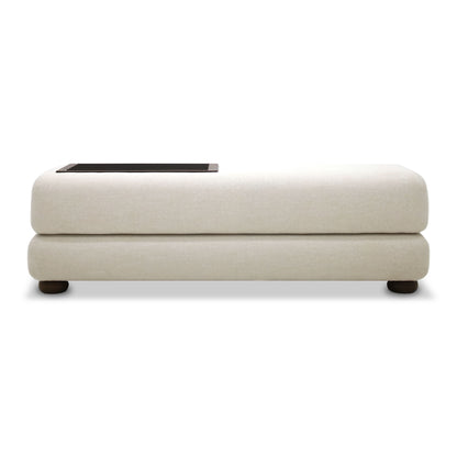 Le Banc de lit Suite de Humble Nature est un pouf beige moderne et minimaliste avec un plateau rectangulaire foncé à une extrémité, avec des tissus somptueux pour une touche luxueuse. Il présente une surface lisse et rembourrée et est élégamment soutenu par de petits pieds noirs ronds.