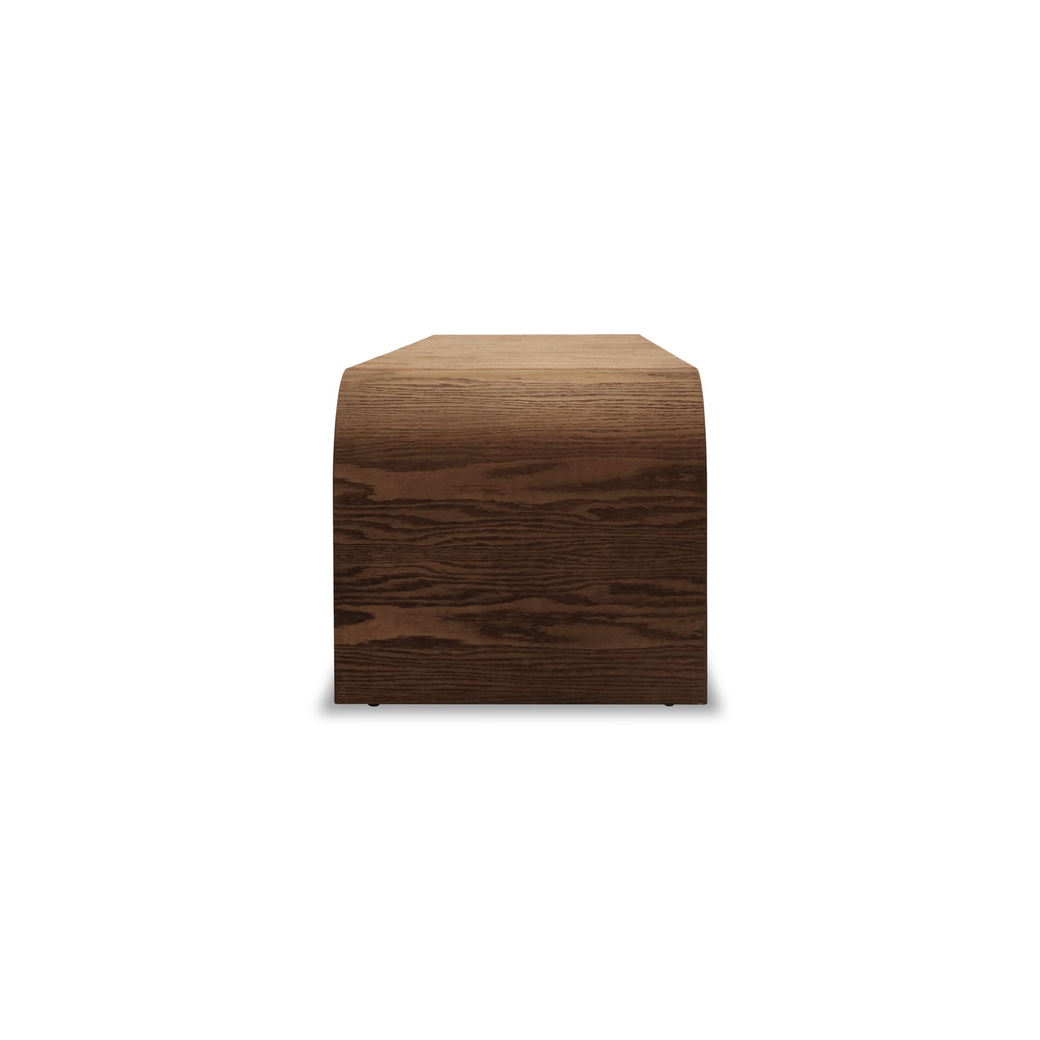 Le Banc 64 en bois Essence │ PECAN de Humble Nature est un banc en bois minimaliste au design lisse et incurvé. Fabriqué en bois de teinte foncée, il présente une structure simple en forme de bloc sur fond blanc.