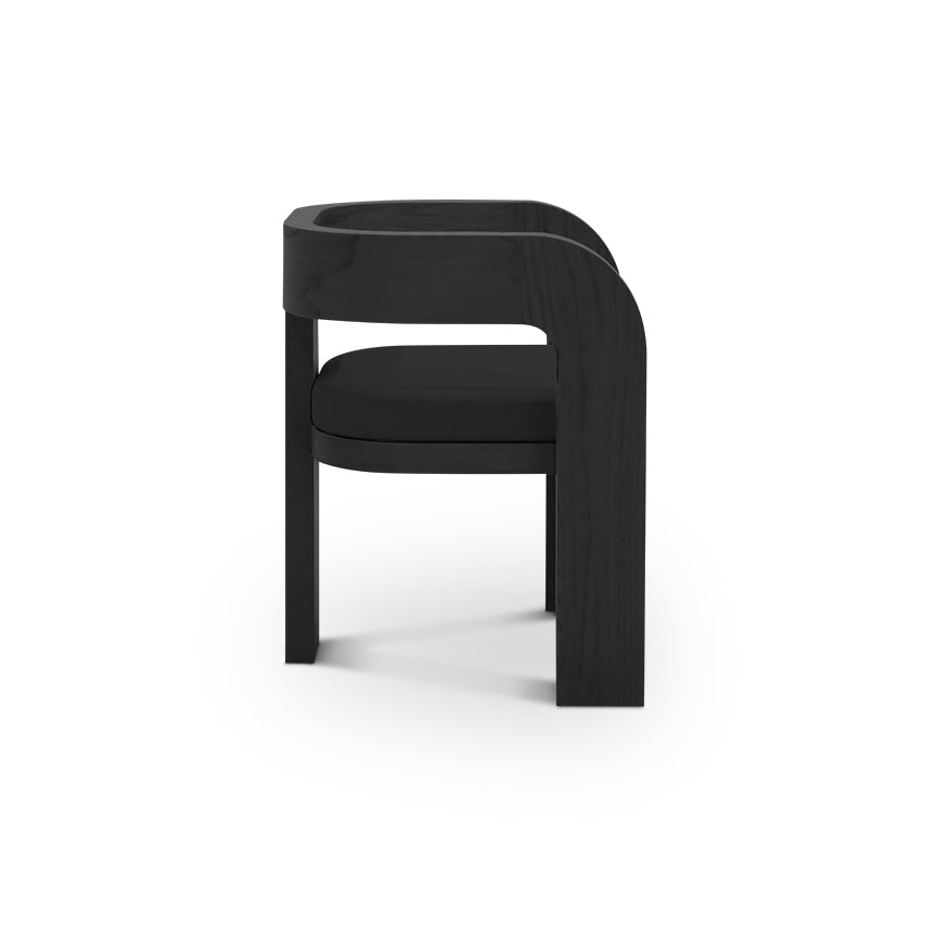 La Chaise de salle à dîner en bois Origin | ONYX de Humble Nature est représentée de profil sur un fond blanc. Ce fauteuil noir moderne et minimaliste est doté dun dossier incurvé et dun coussin noir élégant, soutenu par deux pieds avant verticaux et un pied arrière incurvé, mettant en valeur un savoir-faire exceptionnel.