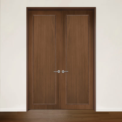 La Porte double CONTOUR en noyer de Humble Nature présente des portes doubles fermées en bois avec des poignées argentées sur un mur blanc sur un sol en bois lisse. Son design moderne et écologique présente des panneaux verticaux subtils fabriqués à partir de bois recyclé.