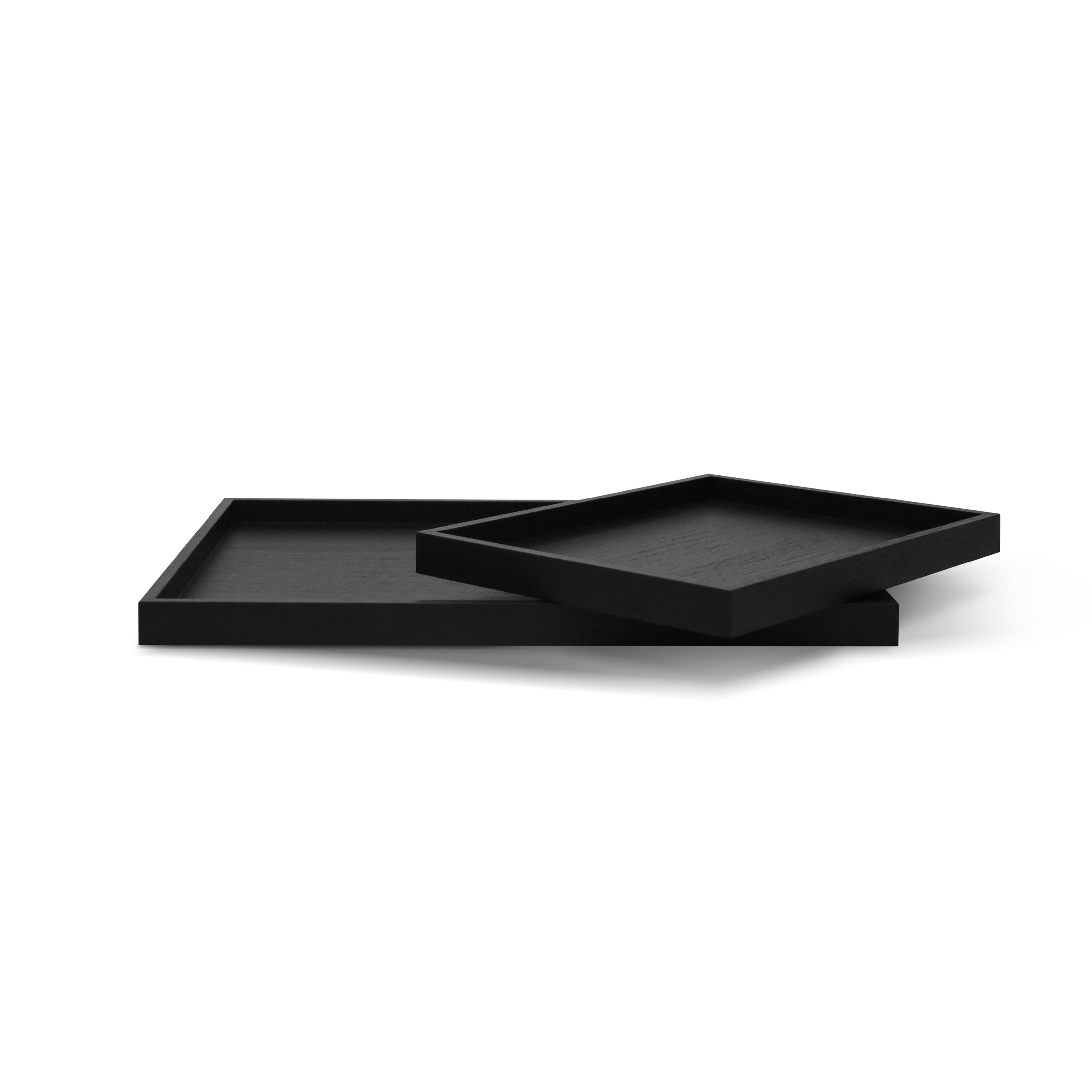 Lensemble de plateaux de bois | Onyx de Humble Nature présente deux plateaux rectangulaires noirs empilés en biais sur un fond blanc. Leur design minimaliste, leur surface lisse et leur touche de rusticité ajoutent de la sophistication, ce qui en fait un ajout élégant à tout décor.