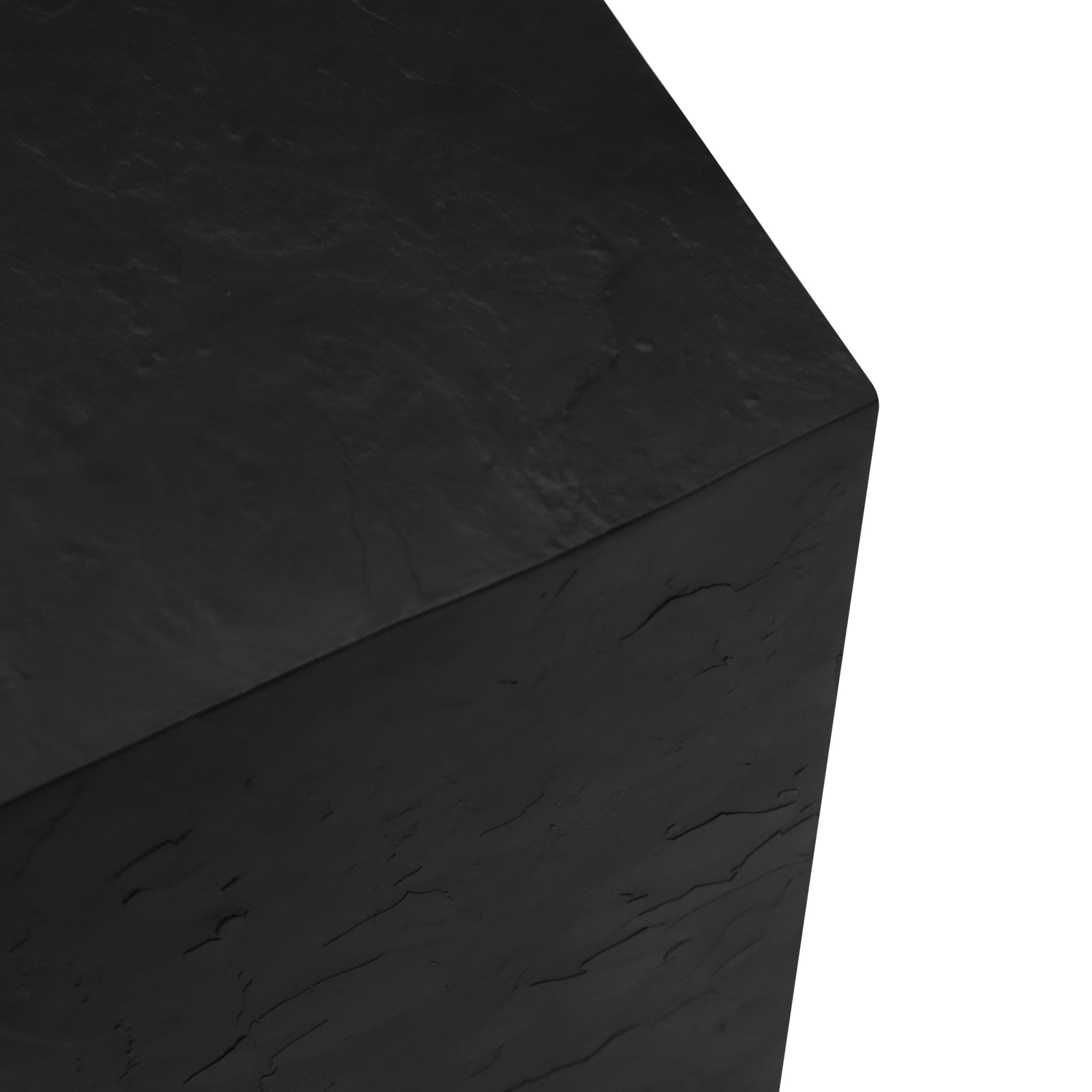 Gros plan dun objet noir en forme de cube avec une surface texturée comme la pierre sculpturale qui met en valeur les coins et les bords sur un fond blanc. De la collection ENSEMBLE DE TABLES PIÉDESTALES EN BOIS FINI PIERRE NATURELLE | ONYX de Humble Nature.