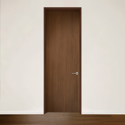 La Porte Pure en noyer de Humble Nature, avec son design épuré en bois et sa poignée argentée minimaliste encastrée dans un mur blanc, respire la qualité artisanale. La lumière naturelle met en valeur la texture lisse de la porte, tandis que le bois assorti au sol ajoute à la cohésion du design.