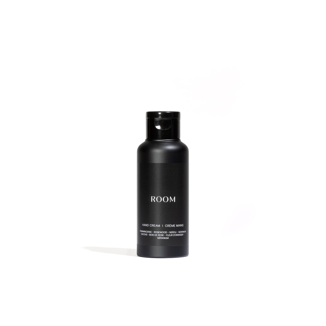 Une élégante bouteille cylindrique noire avec un bouchon étiqueté « ROOM » en texte blanc affiche le produit « Crème enrichie pour les mains entièrement naturelle │ ÉCHANTILLON » de Leroy Williams x Humble Nature, sur un fond blanc uni.