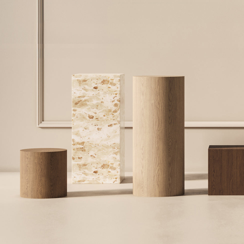 Quatre TABLES PIÉDESTALES EN PIERRE NATURELLE MOYENNES | CAPRI de Humble Nature, présentant à la fois des textures de pierre marbrée et de bois lisse dans des tons clairs et foncés, sont disposées de manière artistique contre un mur uni.