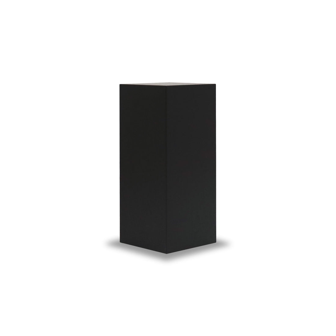 Sur un fond blanc uni, une grande boîte rectangulaire noire, rappelant le piédestal carré 28 Essence en onyx de Humble Nature, se dresse verticalement, projetant une ombre subtile à sa base. Fabriquée en matériaux naturels, elle évoque un design minimaliste.