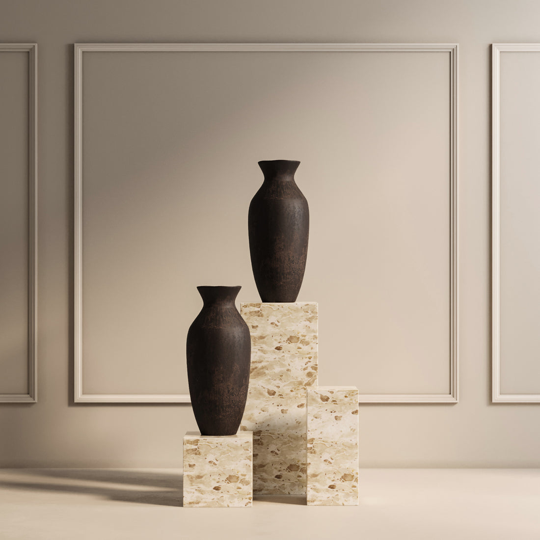 Deux grands vases sombres sont élégamment présentés sur un trio de TABLE PIÉDESTALE EN PIERRE NATURELLE EXTRA LARGE | CAPRI de Humble Nature de différentes hauteurs, placés contre un mur de couleur neutre élégamment encadré pour un look minimaliste et sophistiqué.