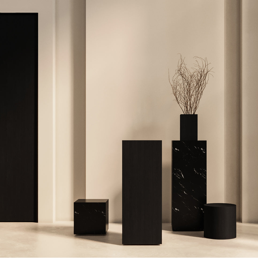 Intérieur minimaliste avec des piédestaux noirs géométriques sur des murs beiges ; comprend la table Humble Nature, un piédestal carré 41 Essence | Marbre Nero, un haut piédestal cylindrique avec un vase, une colonne rectangulaire moyenne et un petit cube. Fabriqué à partir de matériaux naturels, l&