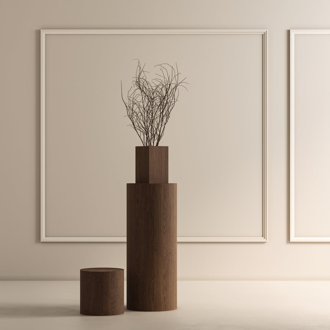 Une pièce minimaliste présente deux guéridons en bois Humble Nature de différentes hauteurs. La Table piédestal circulaire 41 Essence en Pecan, plus haute, supporte un vase aux branches nues contre un mur clair orné de deux cadres rectangulaires vides, soulignant ainsi l&