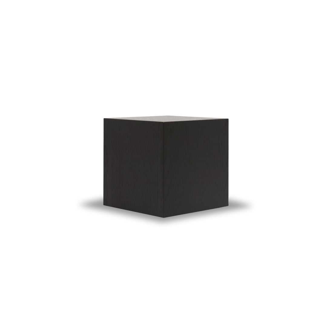 La Table piédestal carré 16 Essence | Onyx de Humble Nature est un cube noir solide au centre d’un fond blanc, ressemblant à une œuvre sculpturale et projetant une ombre douce autour de sa base.