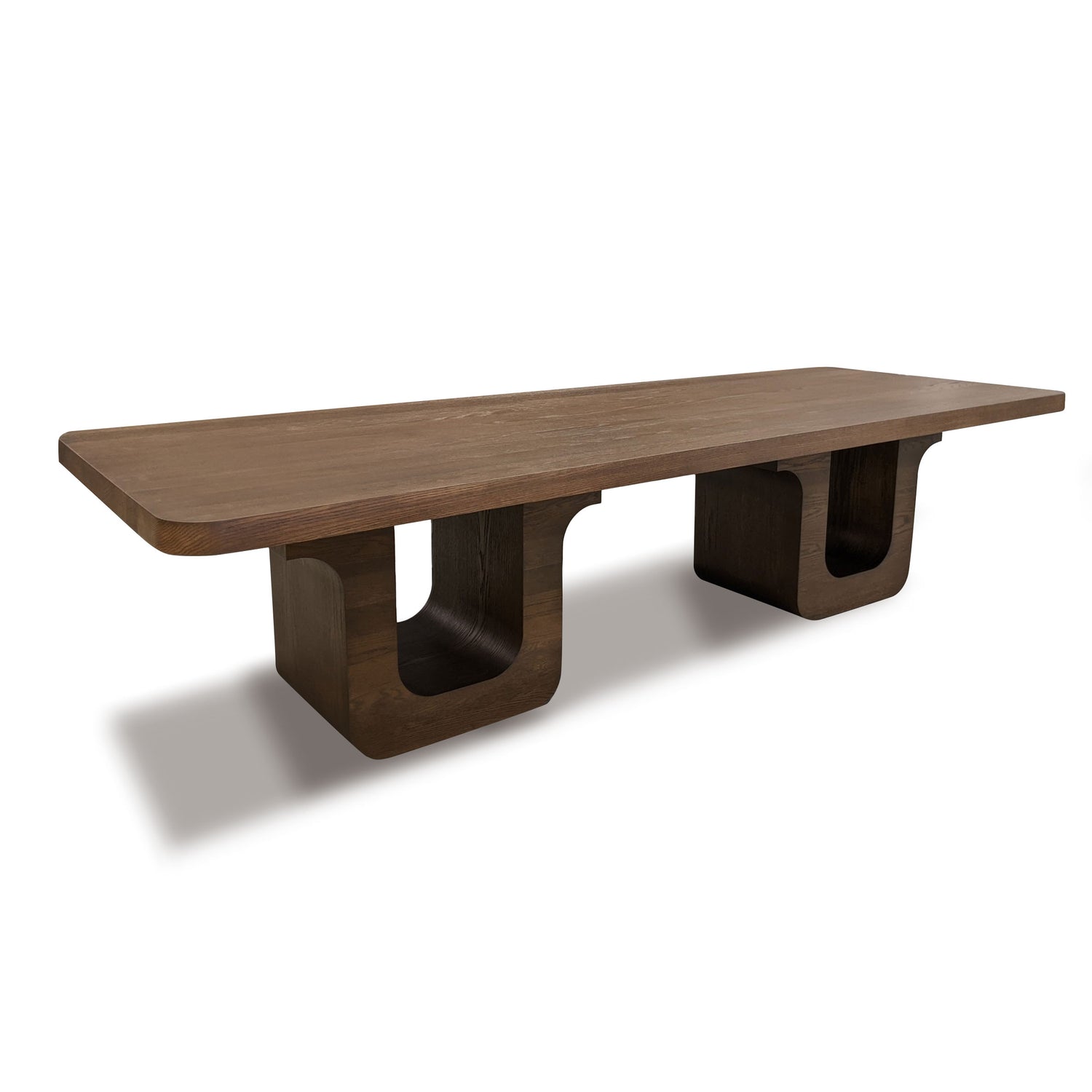 La Table à dîner 120 Suite │ PECAN de Humble Nature est une superbe pièce maîtresse. Cette longue table rectangulaire en bois présente une surface lisse et deux pieds en U, avec une riche finition brun foncé rappelant le placage de chêne rouge, projetant une ombre subtile sur le fond blanc.