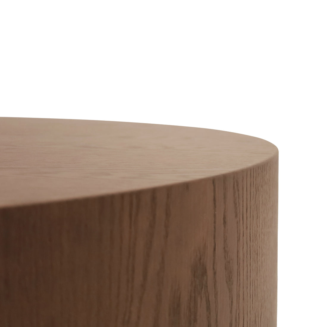 Gros plan de la Table basse circulaire 40 Essence | Saddle de Humble Nature, avec son design cylindrique en bois et sa surface lisse marron clair. Laccent est mis sur son bord arrondi, mettant en valeur la texture du grain du bois et son aspect épuré et moderne sur un fond blanc.