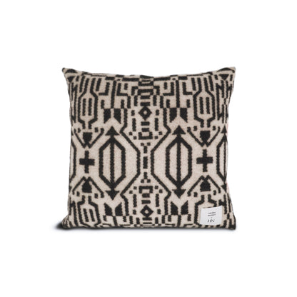 Faisant partie de la collection Amik de Humble Nature, le Coussin en laine de Merino Moyen Amik de CAROLINE MONNET présente un motif géométrique noir et blanc inspiré des motifs Anishinaabe, avec des formes symétriques et une petite étiquette dans le coin inférieur.