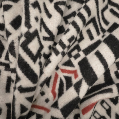 Gros plan dun tissu présentant un motif géométrique abstrait noir et rouge sur fond blanc. Parfait pour le Jeté en laine de Merino Amik de Humble Nature et Caroline Monnet, le motif comprend des formes variées comme des triangles, des rectangles et des zigzags pour un look complexe et dynamique.