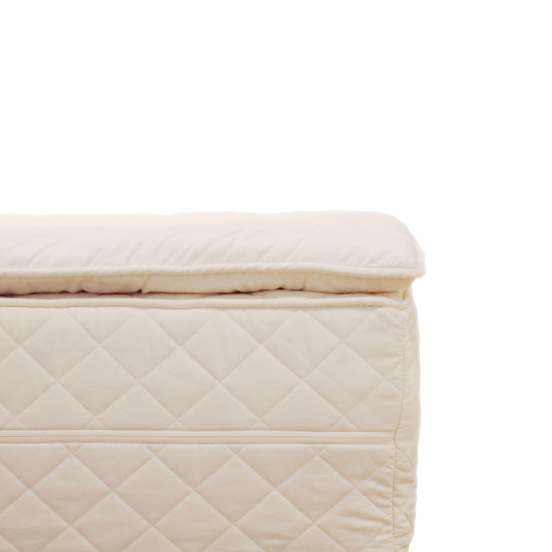 Gros plan dun pouf matelassé beige clair avec surpiqûres en losanges rappelant lEnsemble matelas et surmatelas │ KING par Obasan x Humble Nature. Laccent est mis sur la matière et la texture, mettant en valeur le dessus rembourré et lextérieur doux sur un fond blanc uni.