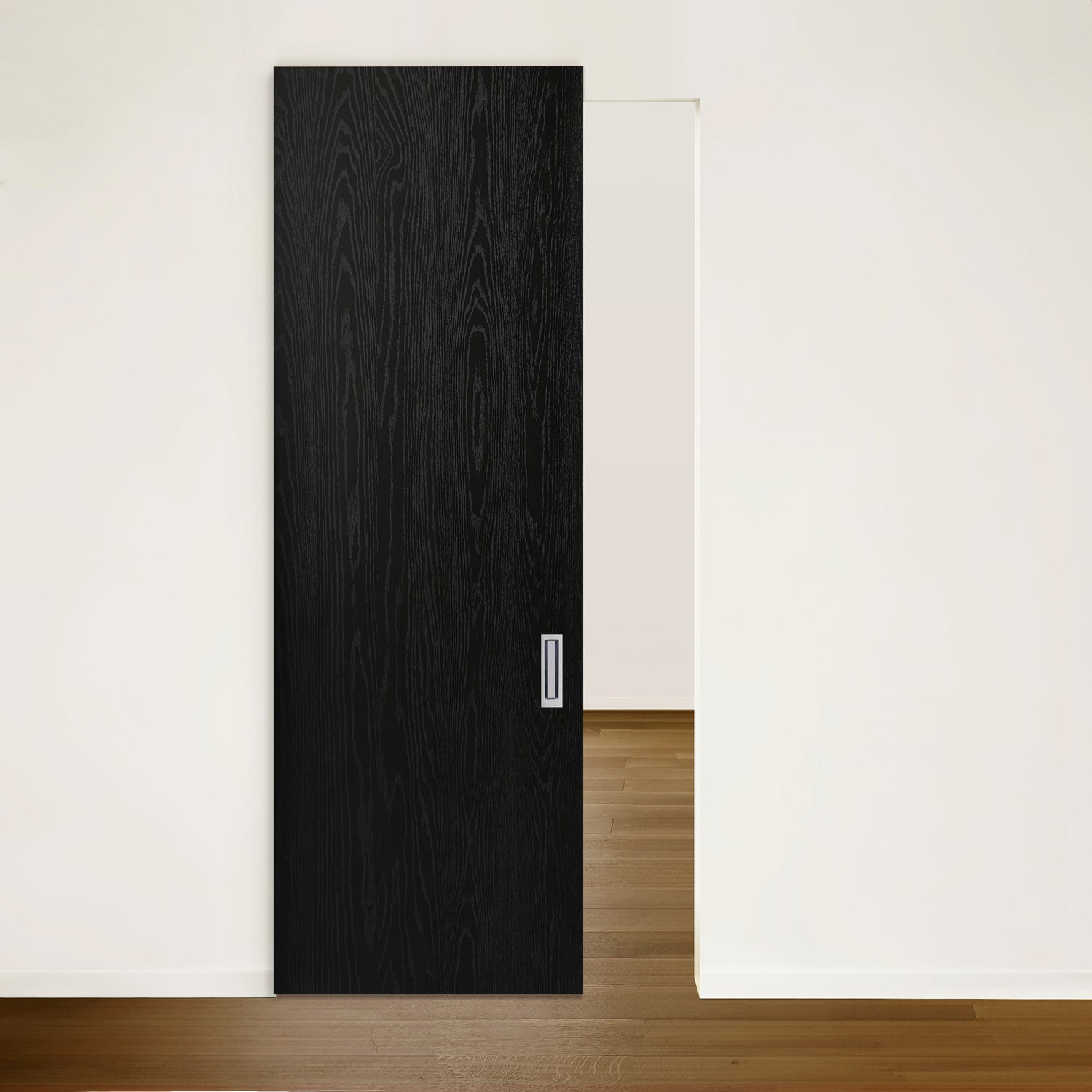 Une Porte Pure coulissante en chêne rouge placage brossé sur dosse Onyx partiellement ouverte en noir élégant de Humble Nature expose une pièce avec un sol en bois clair et des murs blancs. La poignée minimaliste complète parfaitement le décor moderne.