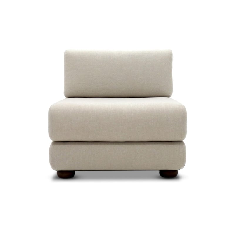 Le canapé Simple Suite de Humble Nature est un fauteuil rembourré sans accoudoirs de couleur crème au design minimaliste moderne. Il est doté dun revêtement lisse et somptueux sur un dossier et un siège rembourrés, posés sur quatre petits pieds ronds en bois sur un fond blanc.